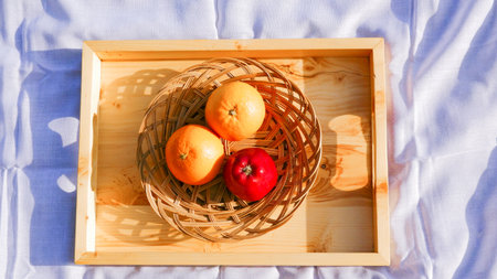Apple and oranges in wooden tray on white napkin. Top view