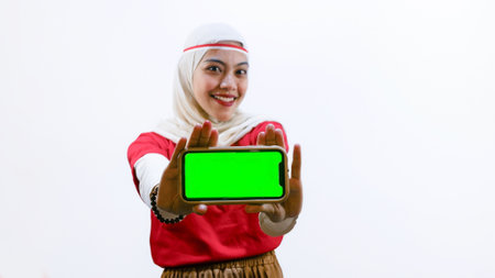 Portrait of Excited young Asian woman celebrate Indonesian independence day on 17 August while holding smartphone with green screen isolated over white backgroundの写真素材