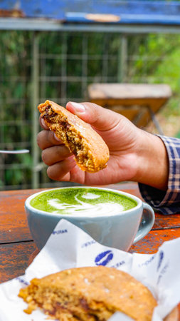 man's hand dipping cookies into green tea latteの写真素材