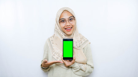 Hijab woman showing smartphone with green screen on white background.