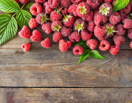 Fresh raspberries with green leaves on wooden background, top view