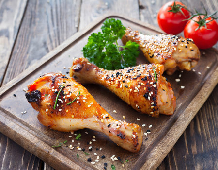 Grilled chicken legs with sesame seeds and parsley on wooden boardの写真素材