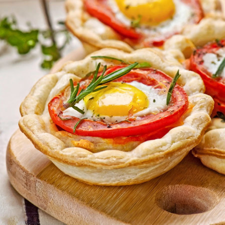 Tartlets with egg, tomatoes and herbs on a wooden boardの写真素材
