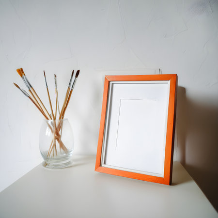 Photo frame and brushes on a white table in a room with a white wall