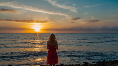A girl in a red dress looks at the sunset over the sea.の写真素材