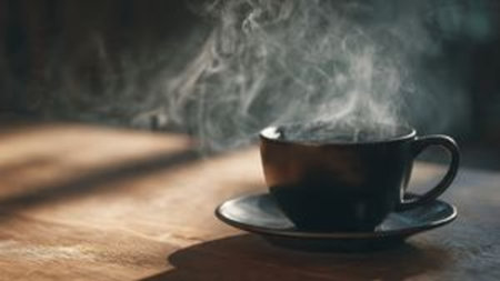 Black cup of coffee on a wooden table in the morning light.