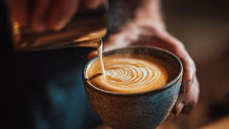 Close-up of barista pouring milk into a cup of coffeeの写真素材