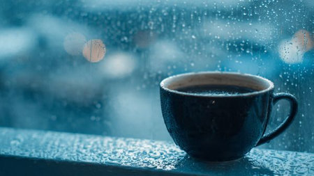 Coffee cup on the window with rain drops and city viewの写真素材