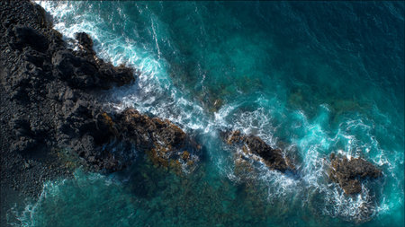 Aerial view of the ocean waves breaking on a rocky shore.