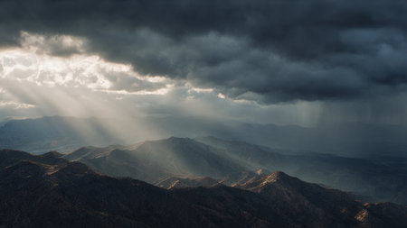 Dramatic sky with sunbeams and clouds over the mountainsの写真素材