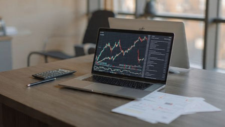 Market fluctuation graphs appear on laptop with supporting documents and coffee.の写真素材