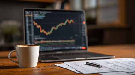 Real-time market indicators glow on a laptop screen while documents and a warm coffee cup complete the workspace.の写真素材