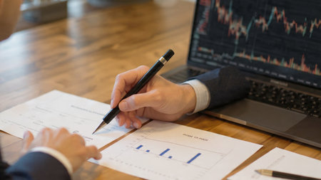Economic indicator graphs fill the laptop screen on a desk decorated with reports and coffee.の写真素材