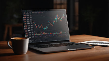 A modern workspace with trading software, financial notes, and warm coffee on a wooden desk.の写真素材
