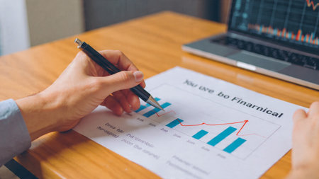 A wooden desk supports a laptop with economic graphs, adding coffee and documents to the analytical scene.の写真素材
