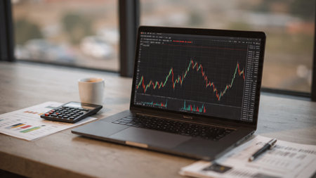 A sleek laptop with stock fluctuations sits with documents and coffee on a structured workspace.の写真素材