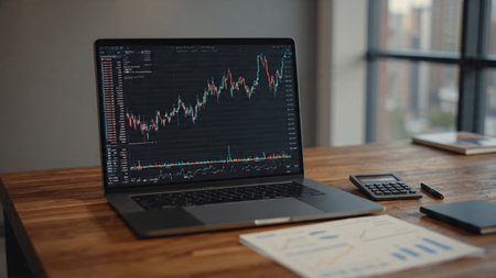 A modern wood-grain desk holds a laptop, market charts, coffee, and printed reports.の写真素材