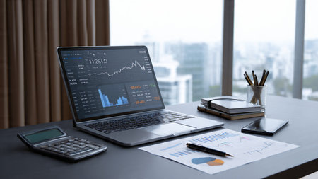 A trading screen glowing on a laptop surrounded by reports and coffee on a wooden surface.の写真素材