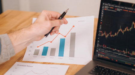 Modern wooden desk showcasing detailed candlestick charts and neatly stacked documents.の写真素材