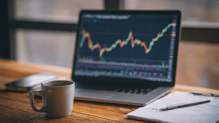 A laptop showing stock performance with organized research papers and a hot beverage on a wooden table.の写真素材