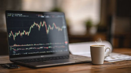 A modern wooden table holding trading dashboard laptop and supportive work documents.の写真素材