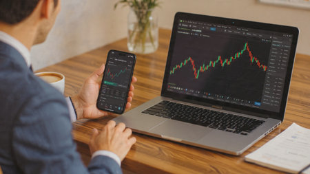 Laptop displaying brightly colored stock lines sits with financial notes and coffee.の写真素材