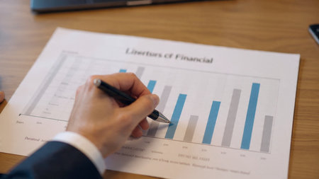 A trading dashboard lights up the laptop while economic reports and a hot coffee sit beside it on a wooden surface.の写真素材