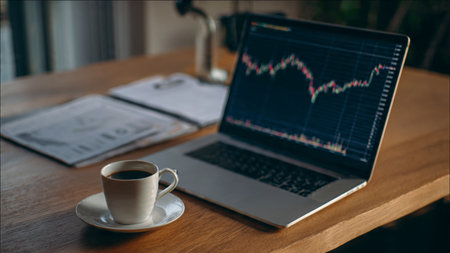 A calm workspace holds a laptop chart display, analysis papers, and fresh coffee.の写真素材
