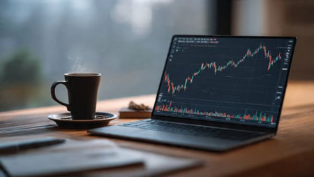 Stock dashboards brighten laptop while papers and coffee add warmth to wooden desk.の写真素材