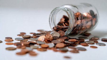 Modern savings perspective showing a tipped jar and coins forming a fan shape, commercial-safe.