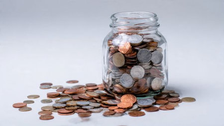 Soft savings composition with a tipped jar and coins flowing neatly across the white surface,...