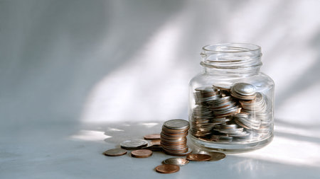 Soft studio-lit arrangement with several coins leading toward a transparent jar, commercial-safe.
