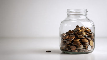 Bright savings aesthetic with coins arranged neatly near a transparent jar on a smooth surface,...