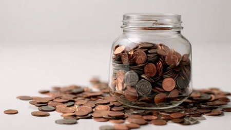 High-key minimalist setup featuring a jar tipped gently as coins spill outward in a soft curve,...