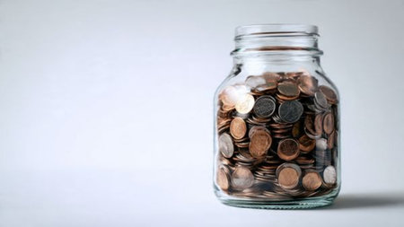 Soft studio-lit arrangement of a jar with coins forming a light circular pattern around it,...
