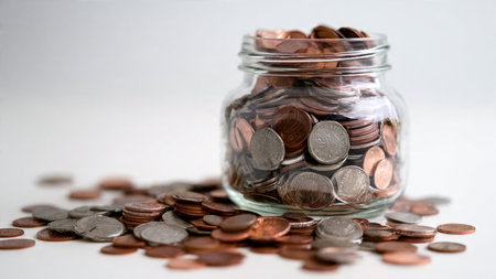 High-key wealth concept with a transparent jar surrounded by loose coins in soft patterns,...