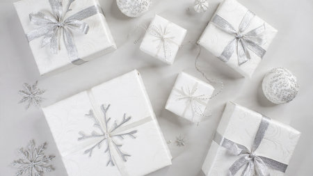White gift boxes with silver ribbons and snowflakes on white background