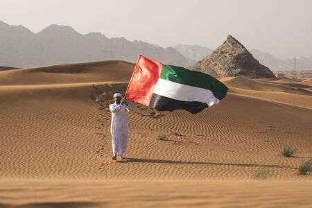 Arab man holding the UAE flag in the desert celebrating UAE national day and Uae flag day.の写真素材