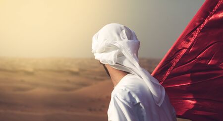 arab man holding flag walking alone in the desertの写真素材