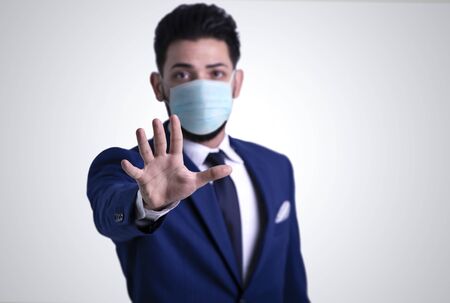 Young man with blue suit showing stop sign with hand, wearing  medical face mask. stop coronavirus concept.の写真素材