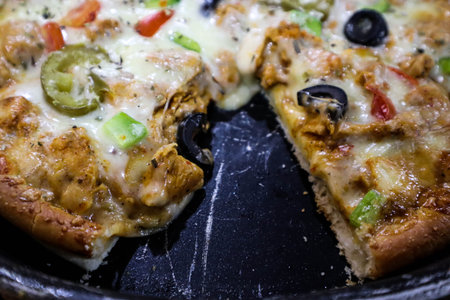 Pizza with chicken, tomato and olives on a black plate