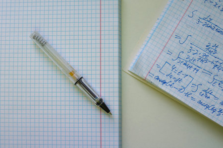 A pen lying on a blank grid notebook next to handwritten mathematical integral equations