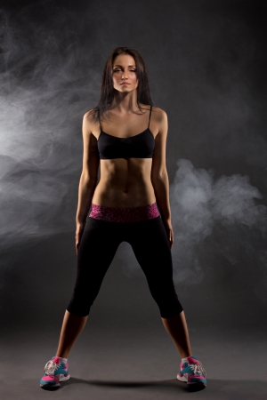 young brunette woman dancer standing on dark background in steamの写真素材