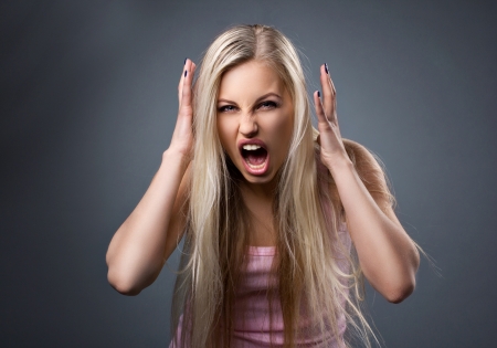 portrait of a crying aggressive girl with blond long hair on dark grey backgroundの写真素材