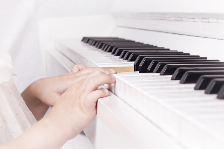 little biautiful girl  playing on white piano unfocussed backgroundの写真素材