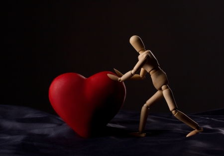 wooden man pushing a red heart on dark on black background