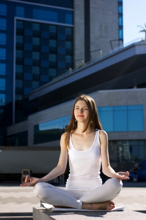 young woman sitting in yoga pose outdoors, on urban backgroundの写真素材