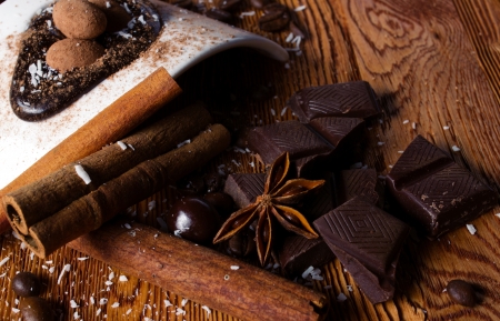 tasty still - heap of  coconut flakes, chocolate, sticks of cinnamon and anise, and white modern plate with brown ball candy on wooden tableの写真素材