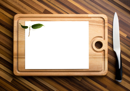 empty white paper with small green leafs learn on carving board, near - steel knife on wooden table