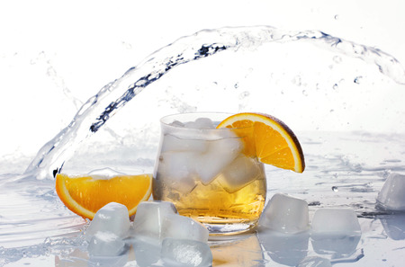 Orange drink with ice and orange slice in glass and water splashes on white backgroundの写真素材